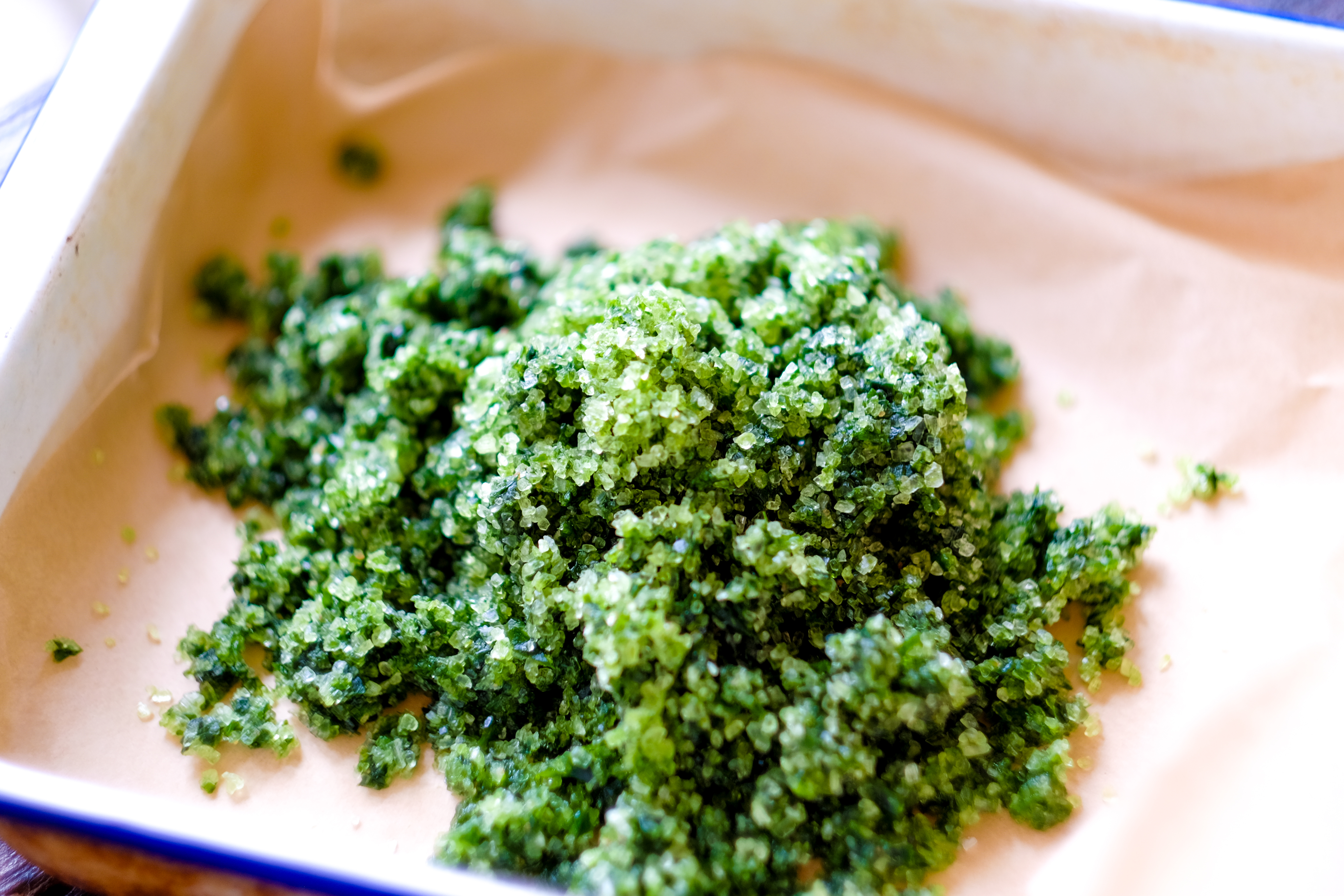 Close-up of green sea salt crystals piled in a dish, sitting on parchment paper.